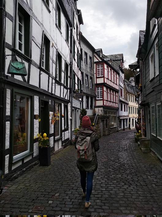 Agatha Makarskas Foto zeigt eine junge Frau mit Rucksack, die die historischen Straßen von Monschau erkundet.